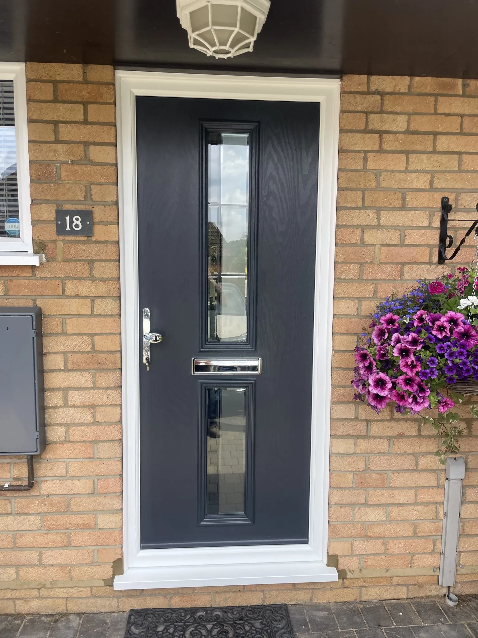 Anthracite grey composite front door with two slim vertical glass panels and chrome furniture, in a white frame on a buff brick house.