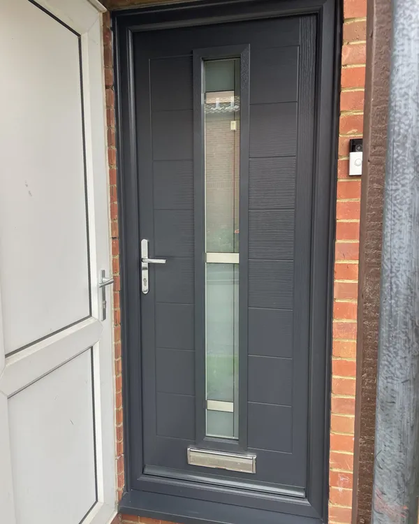Modern anthracite grey composite door with a full-length slim glazed strip and chrome lever handle, in a matching grey frame.