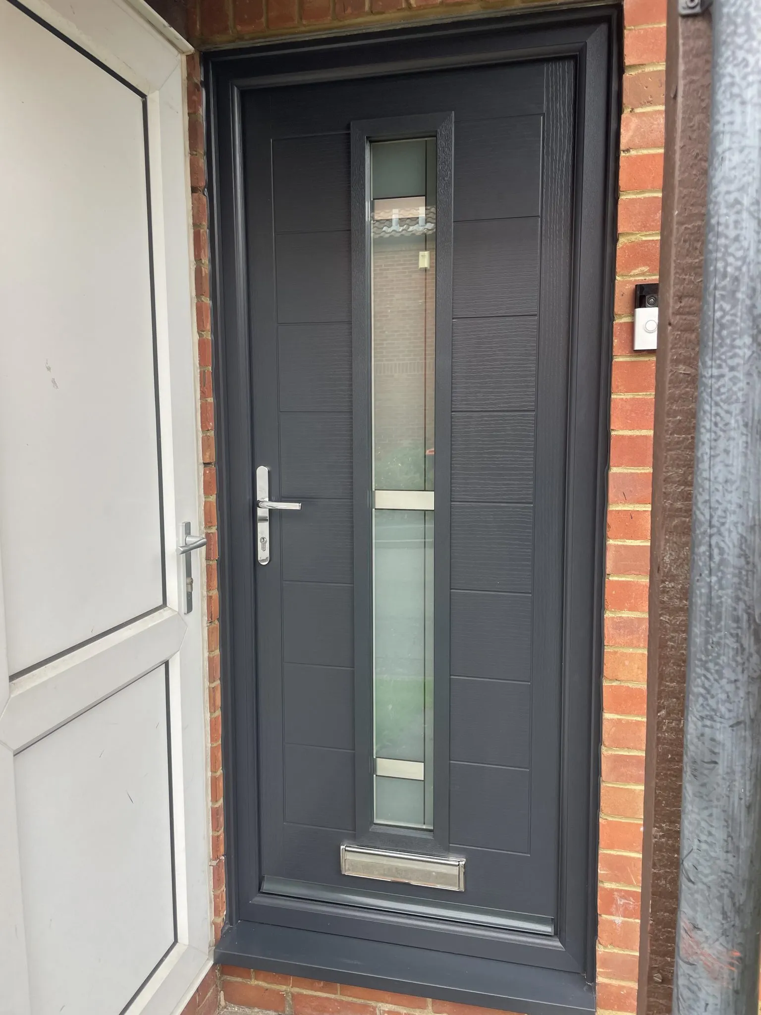 Modern anthracite grey composite door with a full-length slim glazed strip and chrome lever handle, in a matching grey frame.