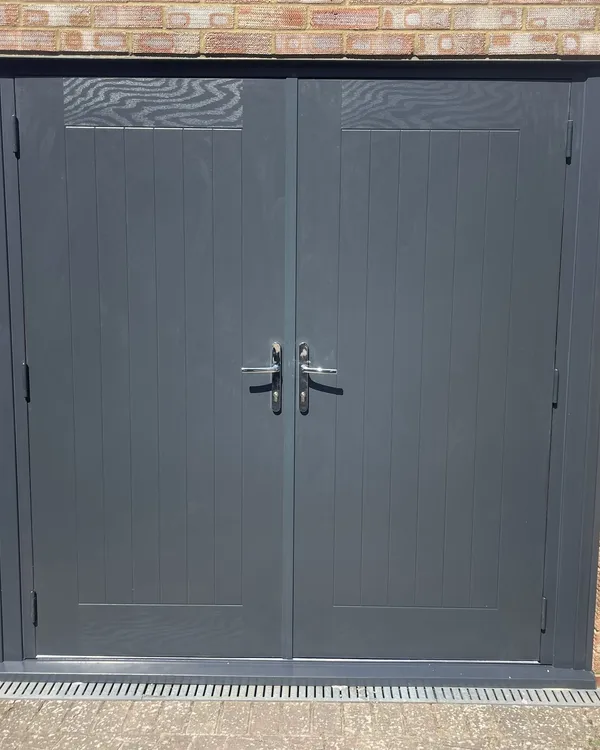 Pair of solid anthracite grey doors with chrome handles fitted across the front of a brick garage.