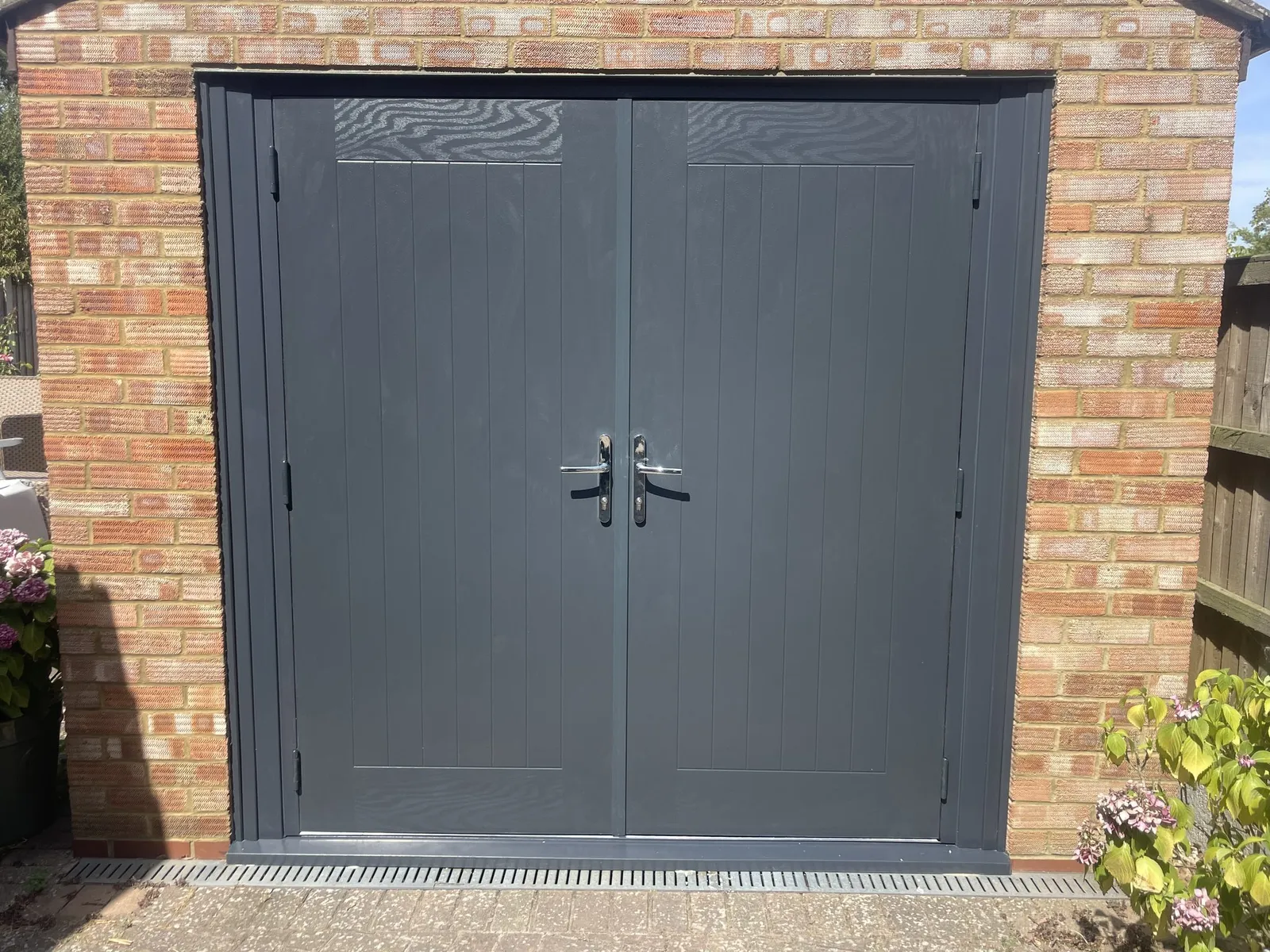 Pair of solid anthracite grey doors with chrome handles fitted across the front of a brick garage.