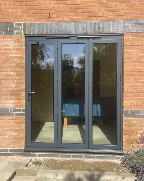 Three-panel anthracite grey bi-fold doors fitted in a red brick wall.
