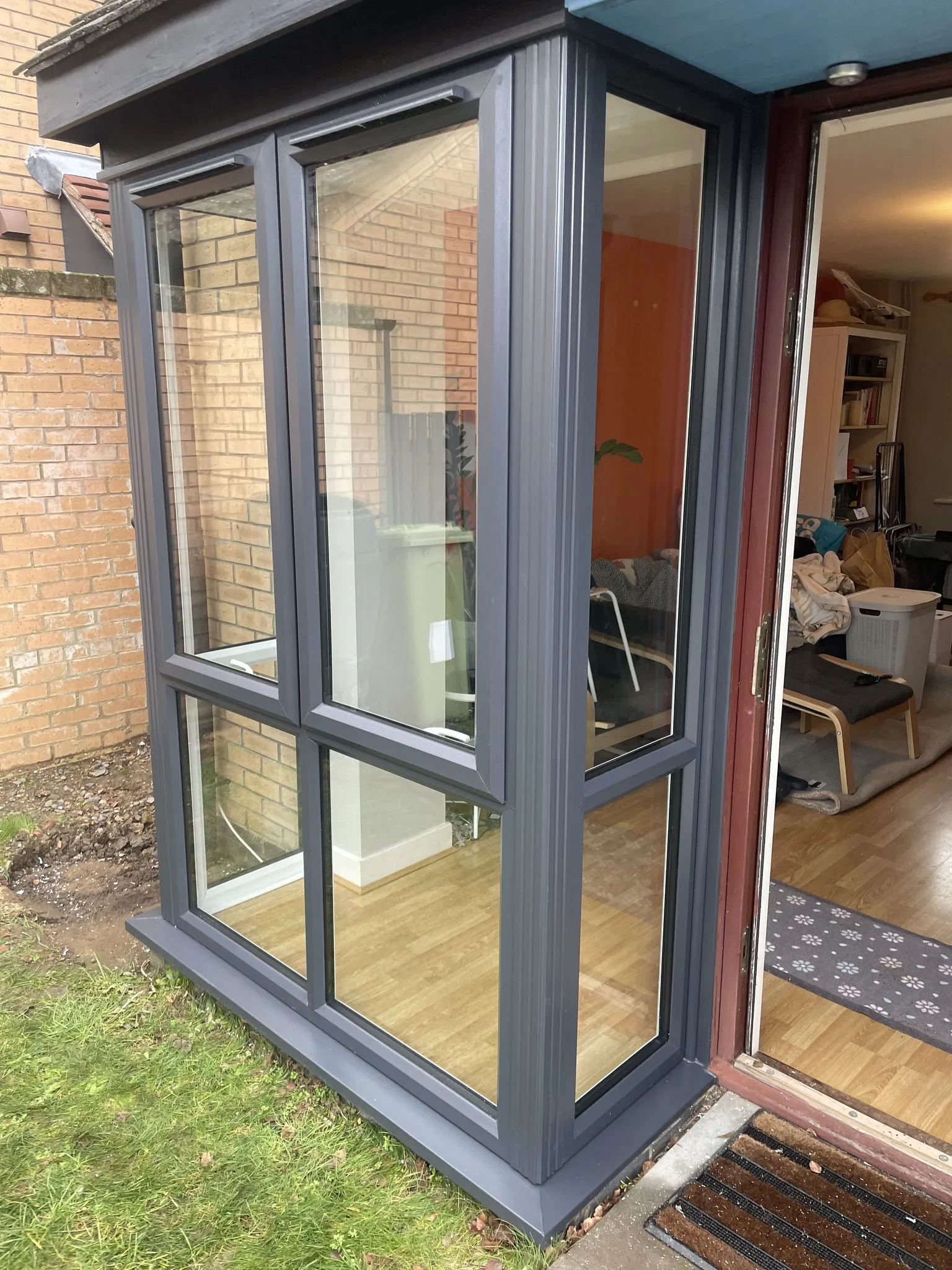 Small anthracite grey uPVC glazed porch with clear glass panels, built against the side of a house.