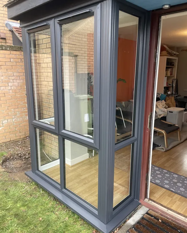 Small anthracite grey uPVC glazed porch with clear glass panels, built against the side of a house.