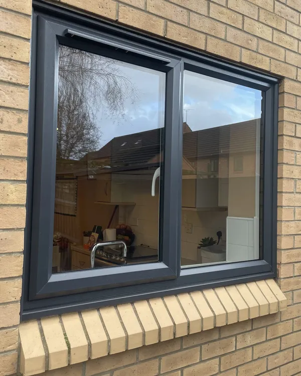 Two-pane anthracite grey uPVC window above a brick soldier-course sill, fitted in a buff brick wall.