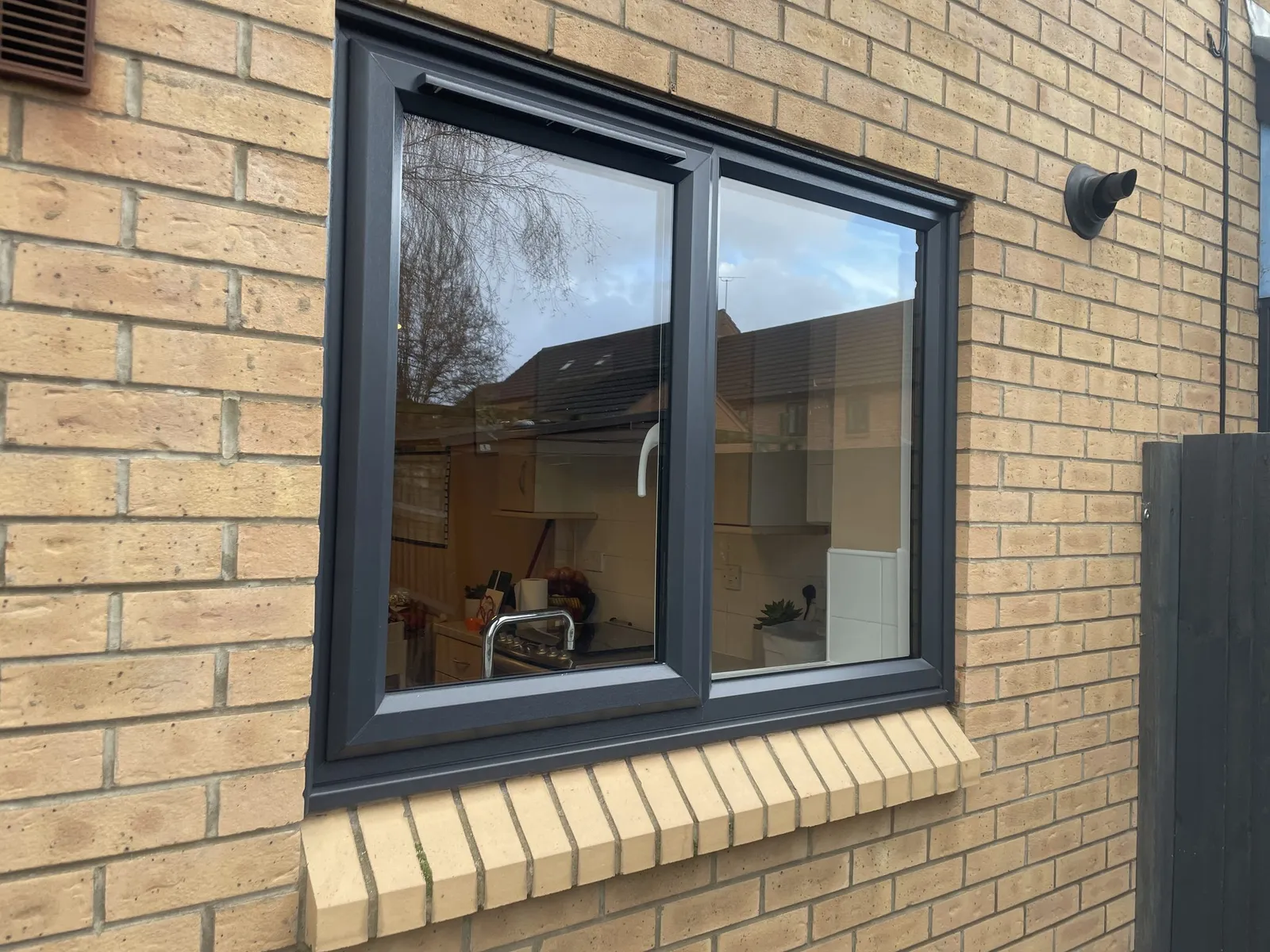 Two-pane anthracite grey uPVC window above a brick soldier-course sill, fitted in a buff brick wall.