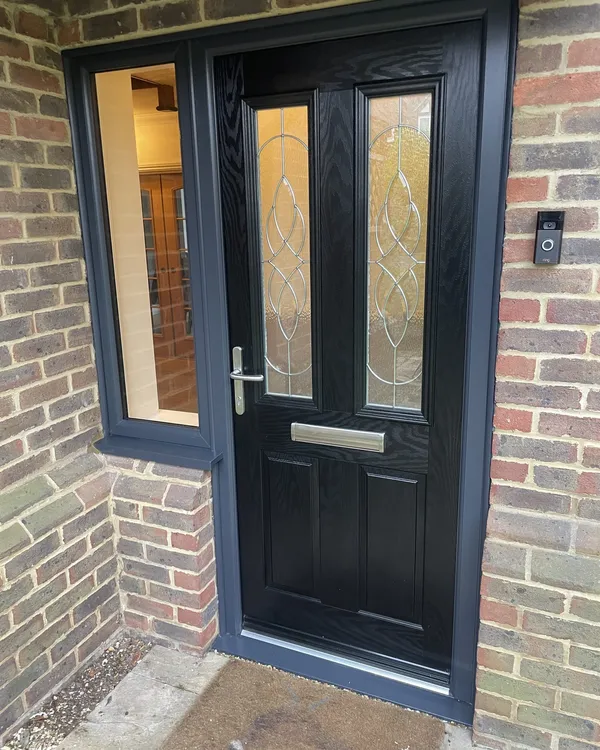 Black woodgrain composite front door with decorative bevelled glass, fitted in an anthracite grey frame with a clear glazed side panel.