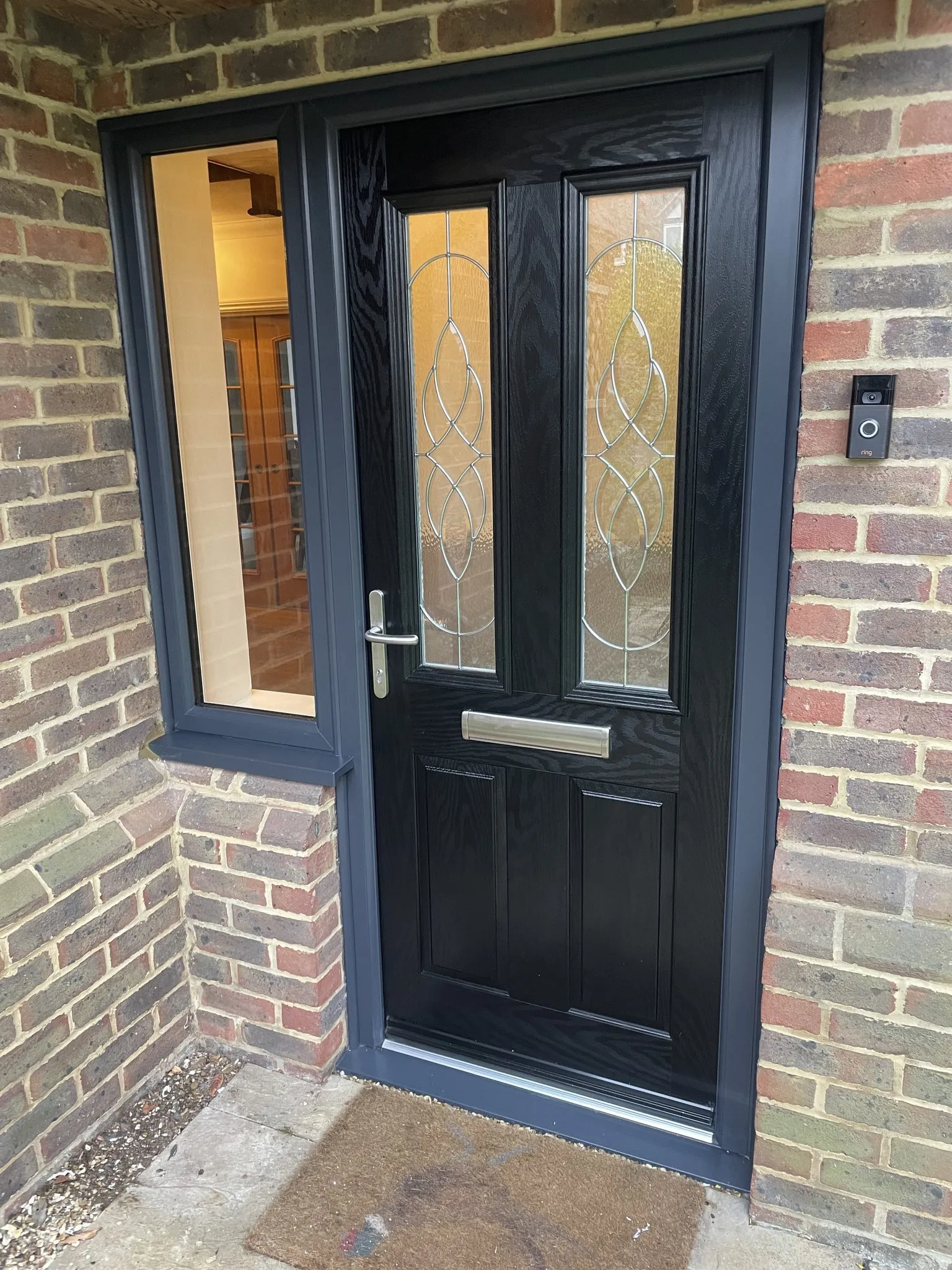Black woodgrain composite front door with decorative bevelled glass, fitted in an anthracite grey frame with a clear glazed side panel.