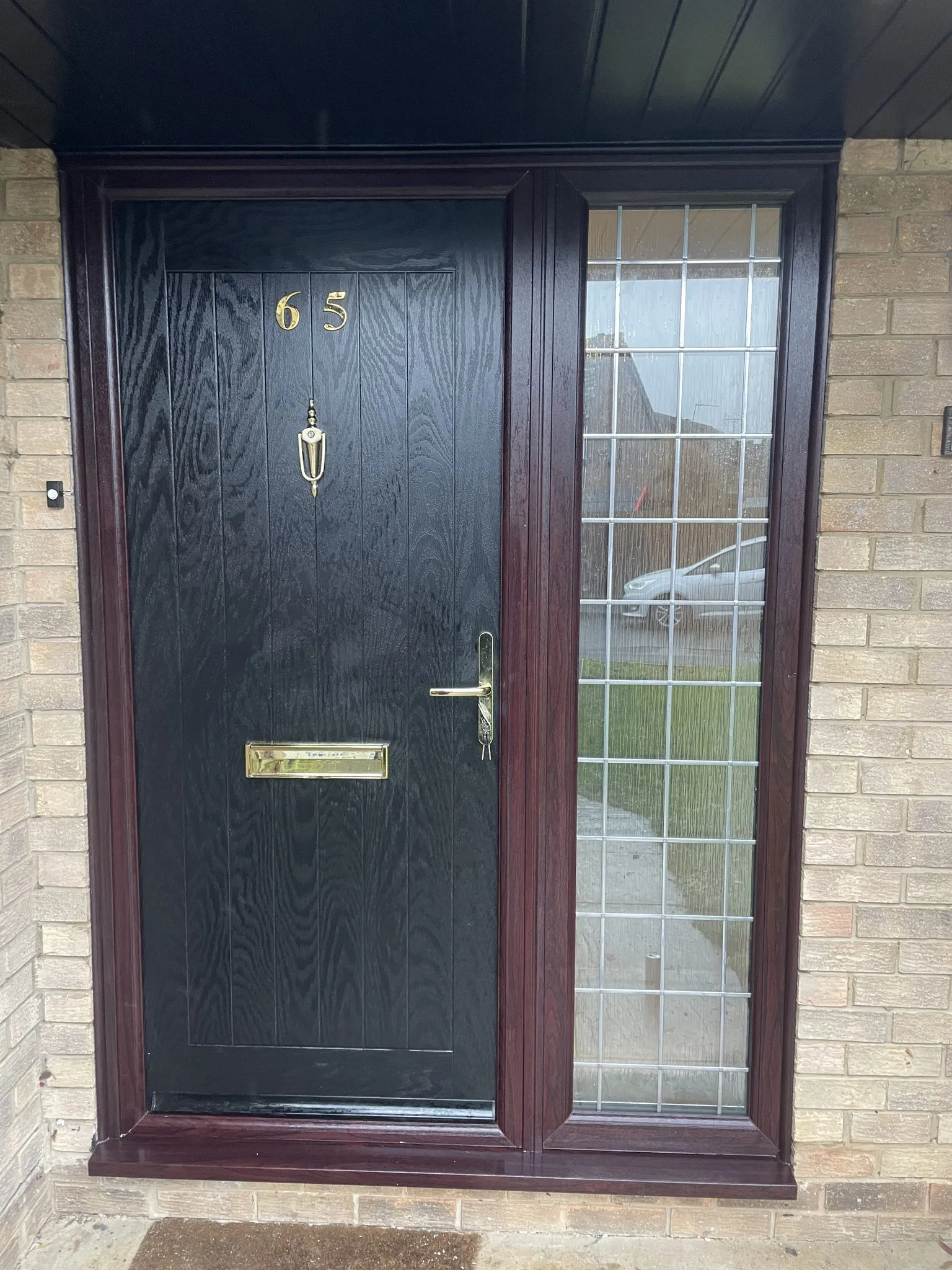 Black woodgrain composite front door with brass numerals, knocker and letterplate, in a rosewood-effect frame with a leaded glass side panel.