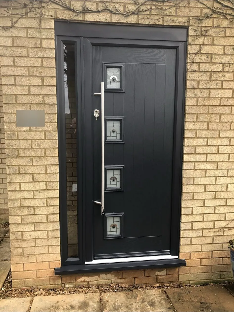 Black composite front door with four small square glazed panels and a long chrome bar handle, in a black frame with a slim glazed side panel.