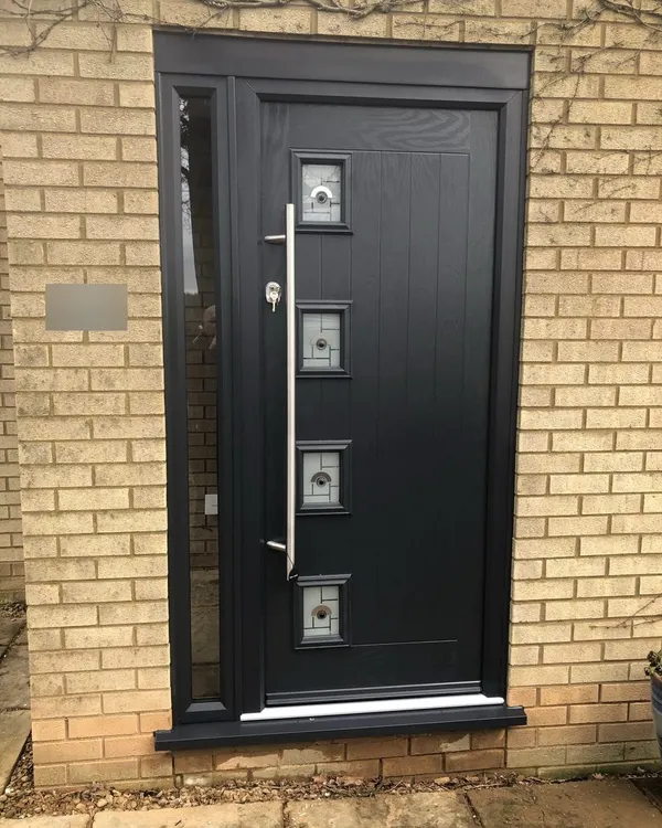 Black composite front door with four small square glazed panels and a long chrome bar handle, in a black frame with a slim glazed side panel.