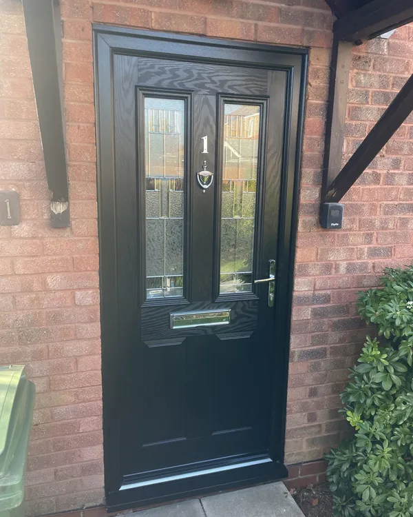 Black woodgrain composite front door with glazed panels, chrome numeral and knocker, in a black frame below a timber canopy.
