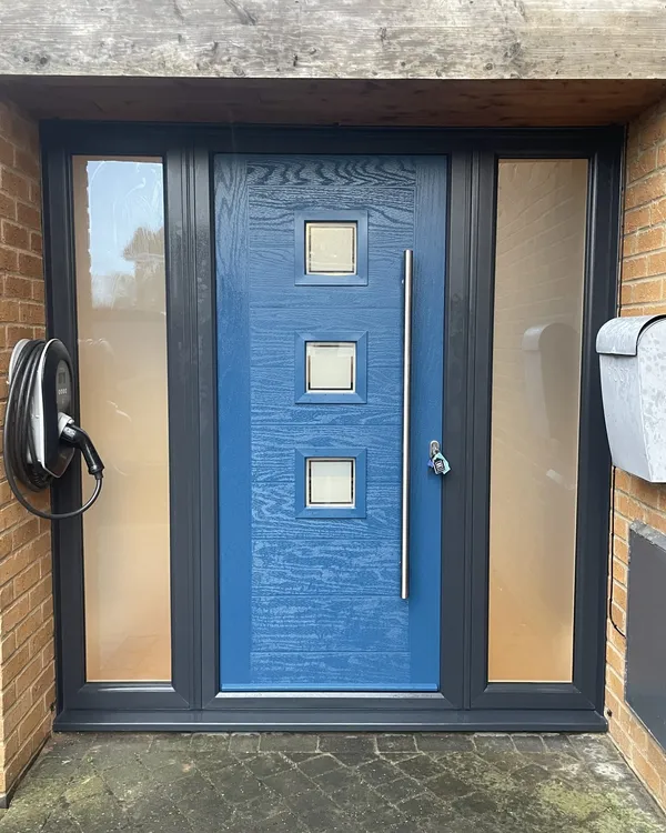 Mid blue contemporary composite door with three square glazed panels and a bar handle, in an anthracite grey frame with obscure side panels.
