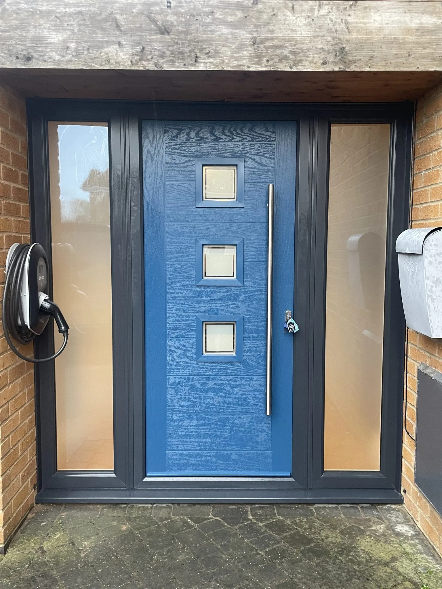 Mid blue contemporary composite door with three square glazed panels and a bar handle, in an anthracite grey frame with obscure side panels.