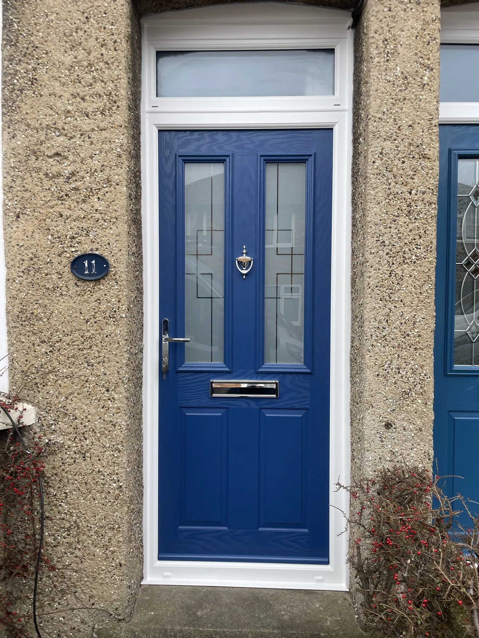 Royal blue composite front door with decorative glass panels and a frosted toplight above, fitted in a pebbledash wall.