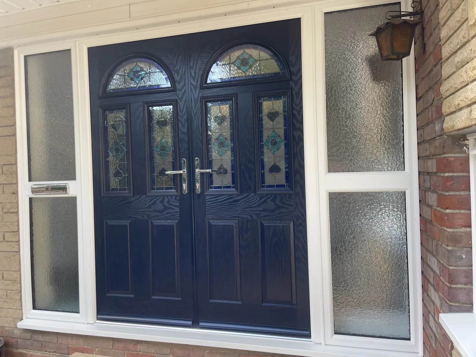 Navy blue composite double front doors with arched stained glass panels, set in a white uPVC frame with obscure glazed side screens.