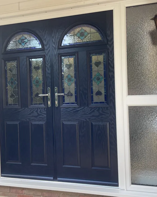 Navy blue composite double front doors with arched stained glass panels, set in a white uPVC frame with obscure glazed side screens.