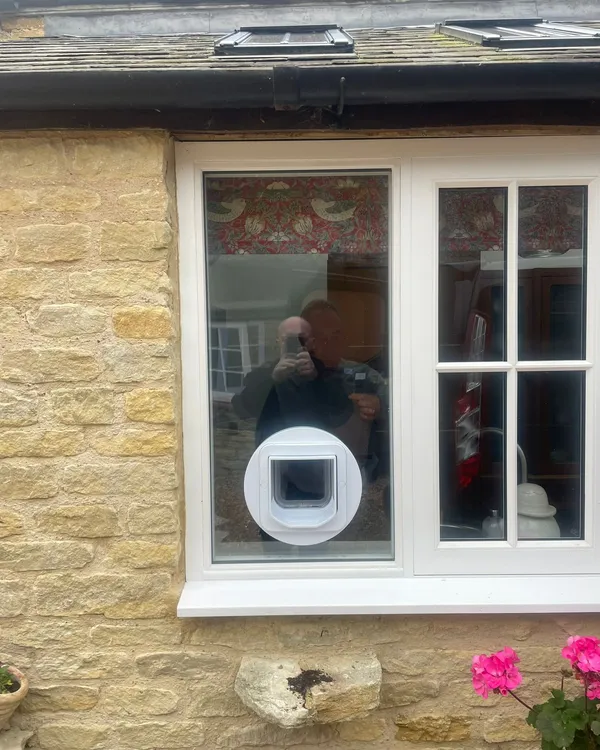 Exterior view of a stone cottage window with a white cat flap neatly set into the glass and a tidy sealed unit surround.