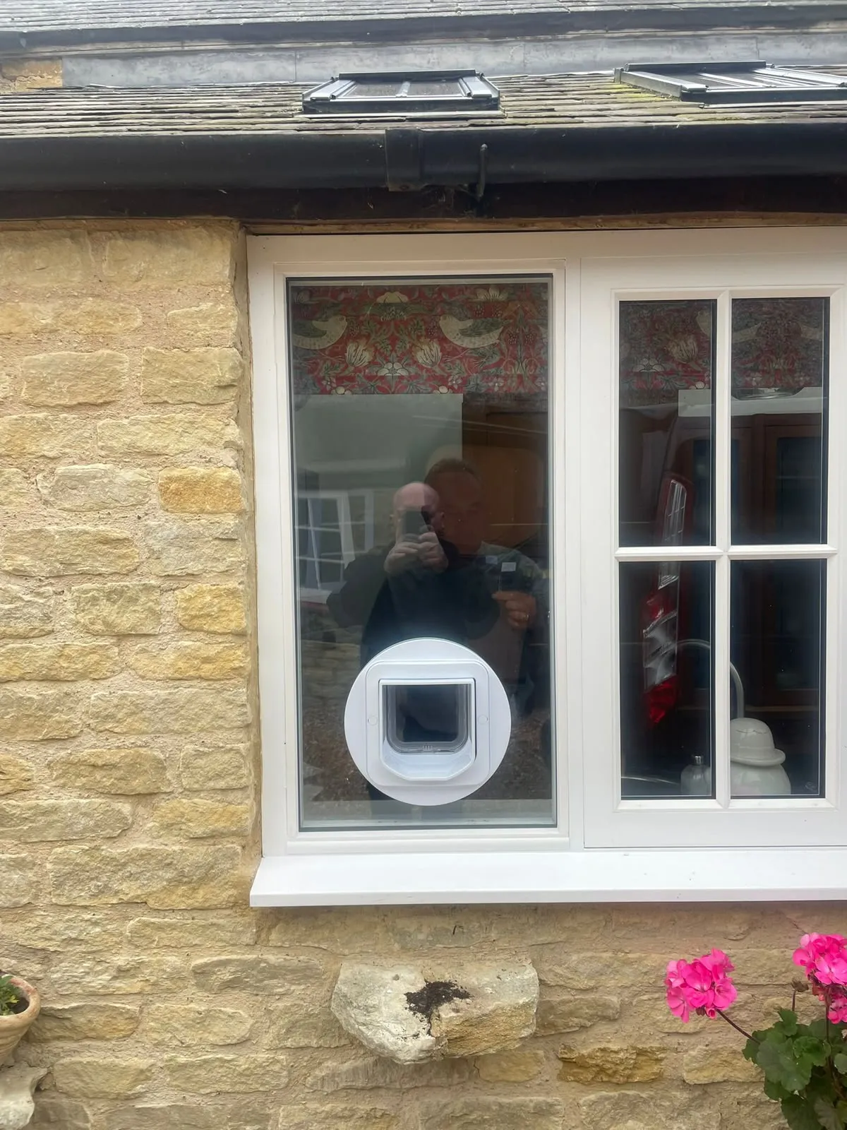 Exterior view of a stone cottage window with a white cat flap neatly set into the glass and a tidy sealed unit surround.