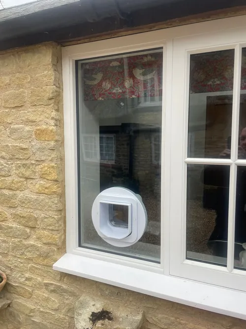 White microchip cat flap fitted into the lower pane of a cottage window in a stone property