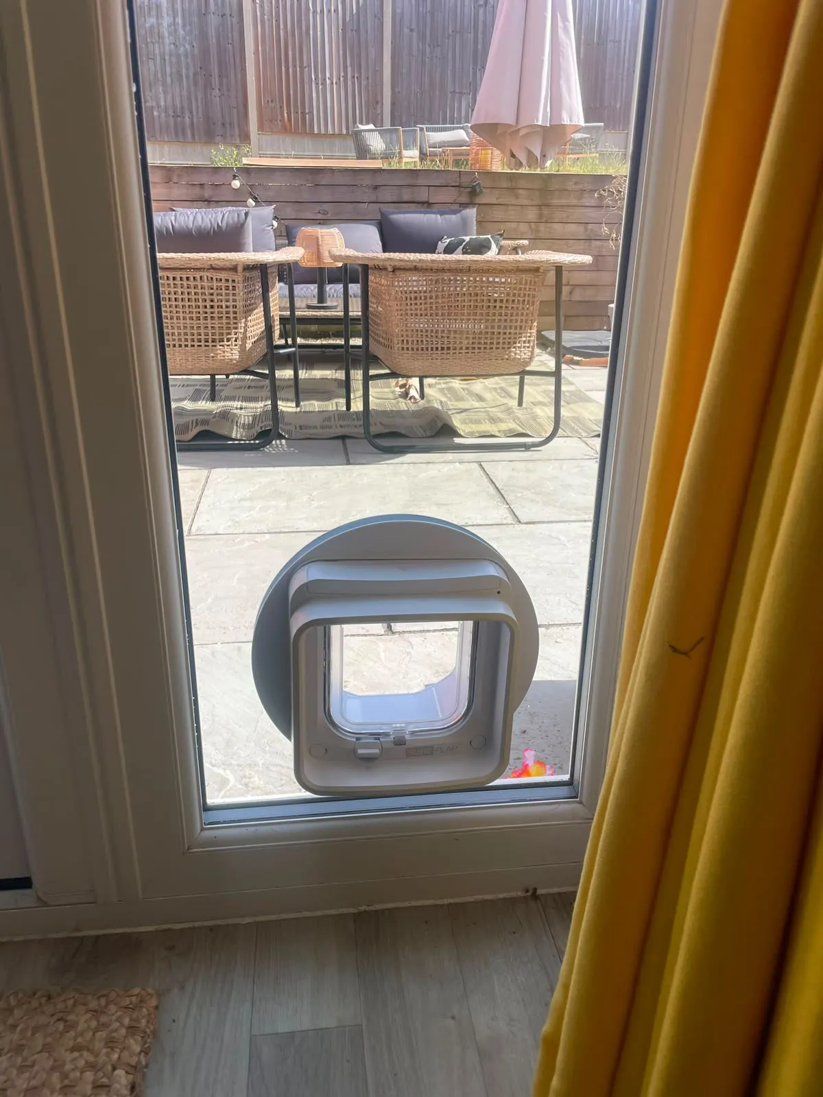 SureFlap DualScan microchip cat flap fitted low in the glazed panel of a uPVC patio door looking out onto a paved garden.