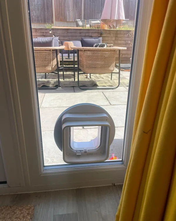 SureFlap DualScan microchip cat flap fitted low in the glazed panel of a uPVC patio door looking out onto a paved garden.