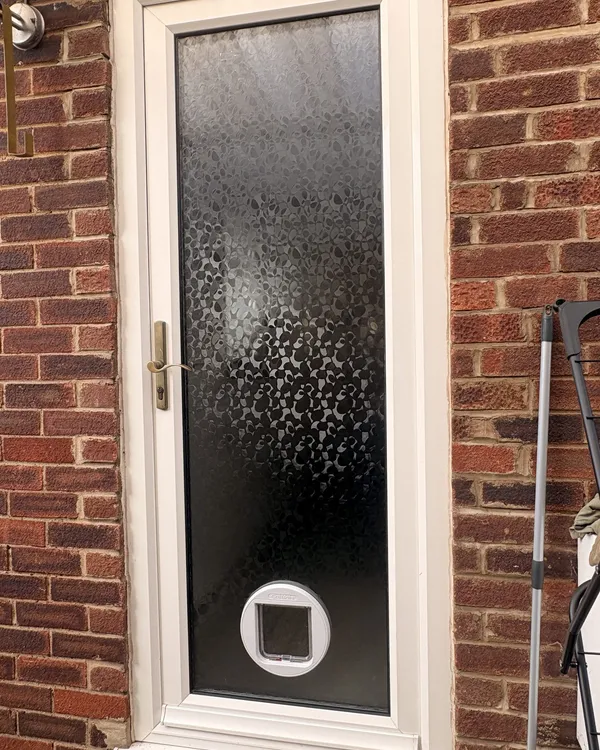 White cat flap fitted low in the full-height decorative obscure glass panel of a white uPVC back door.