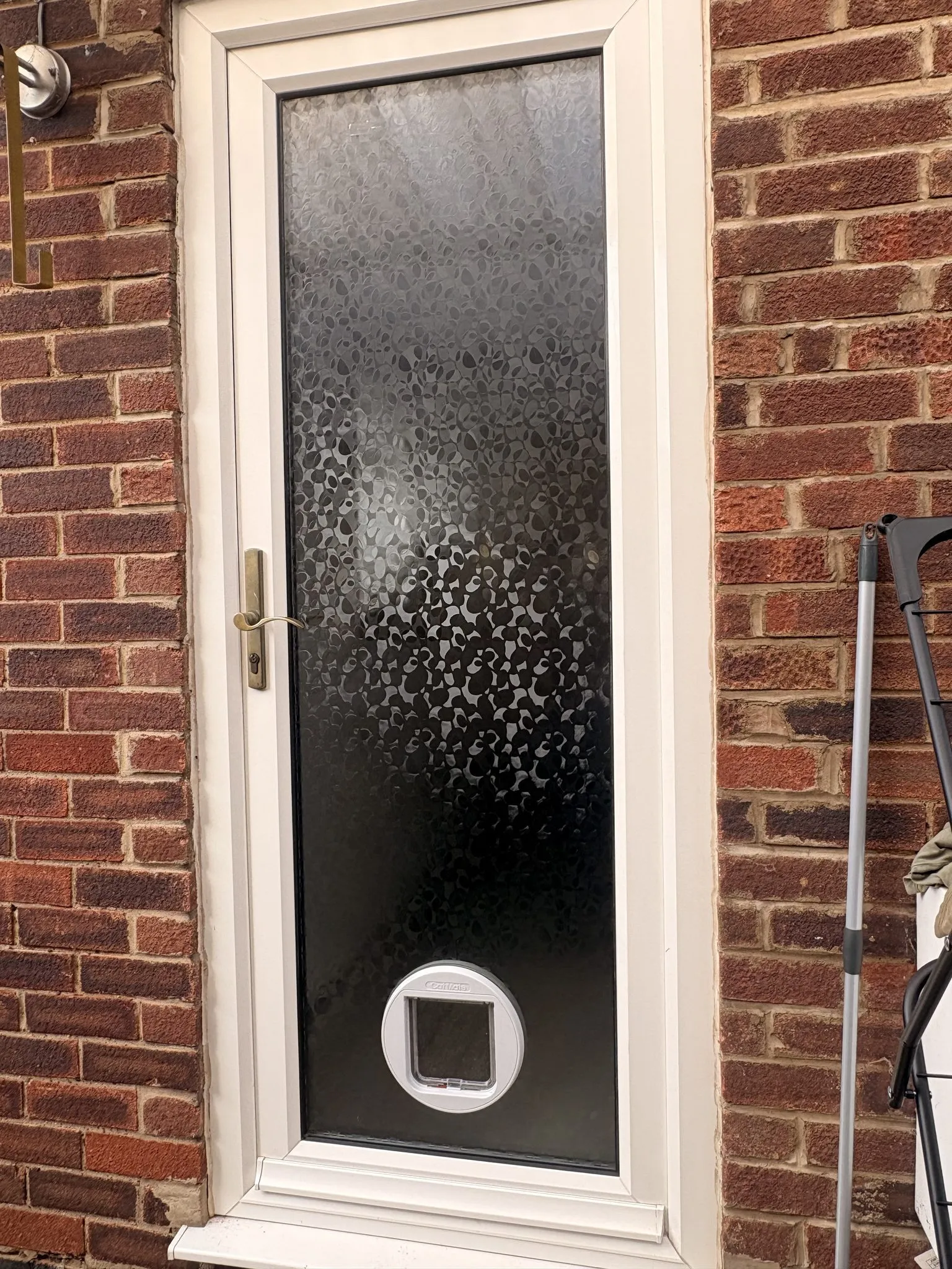 White cat flap fitted low in the full-height decorative obscure glass panel of a white uPVC back door.