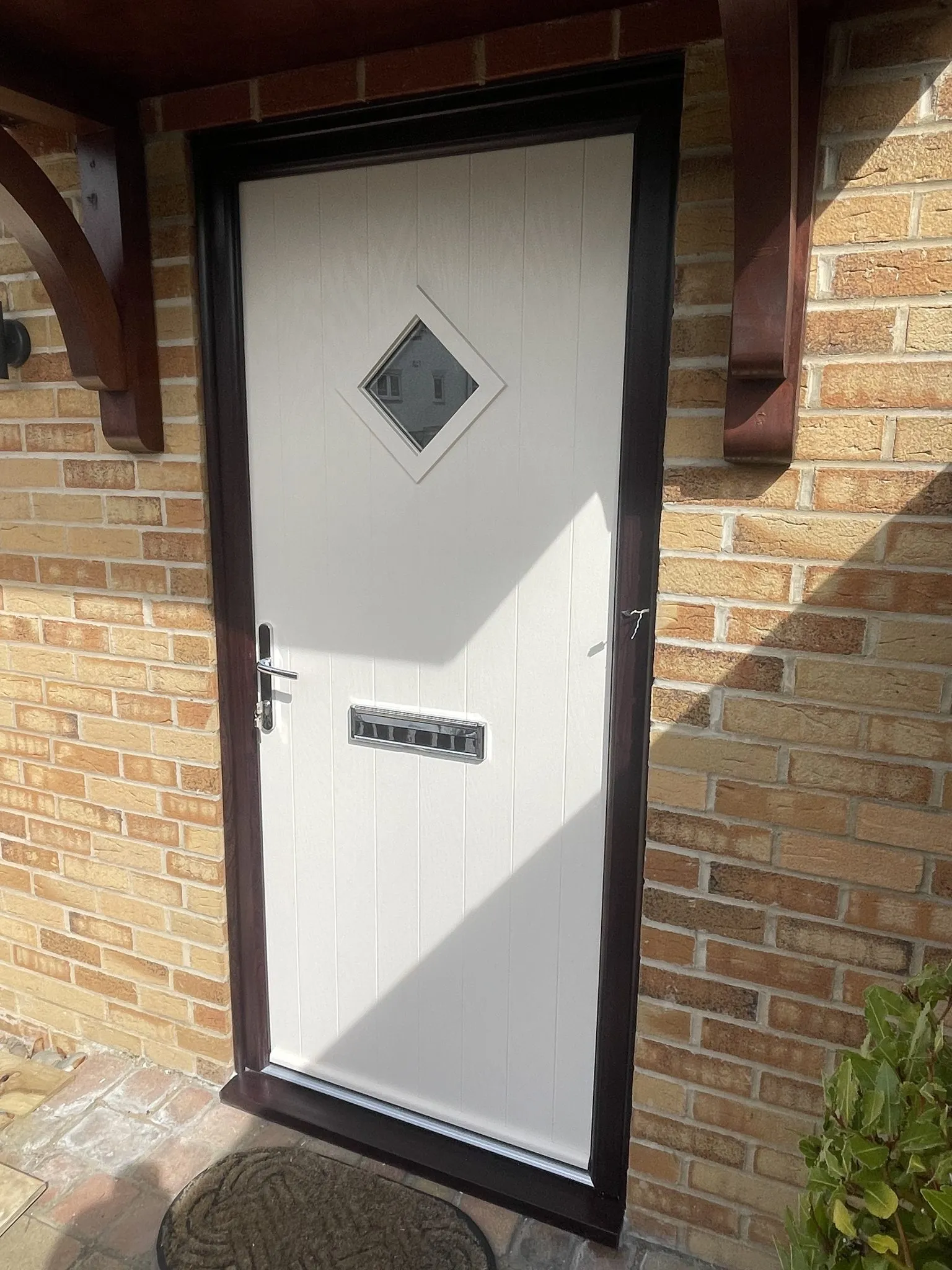 Cream composite front door with a diamond-shaped glass panel and chrome furniture, in a rosewood-effect frame under a timber canopy.
