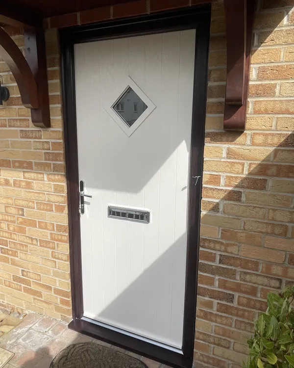 Cream composite front door with a diamond-shaped glass panel and chrome furniture, in a rosewood-effect frame under a timber canopy.
