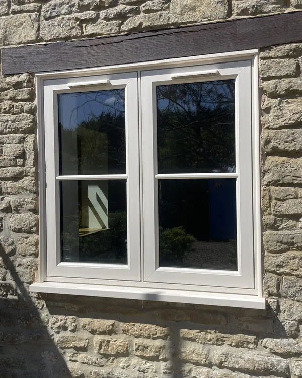 Cream flush casement window with a glazing bar across each sash, fitted in a stone wall under a timber lintel.