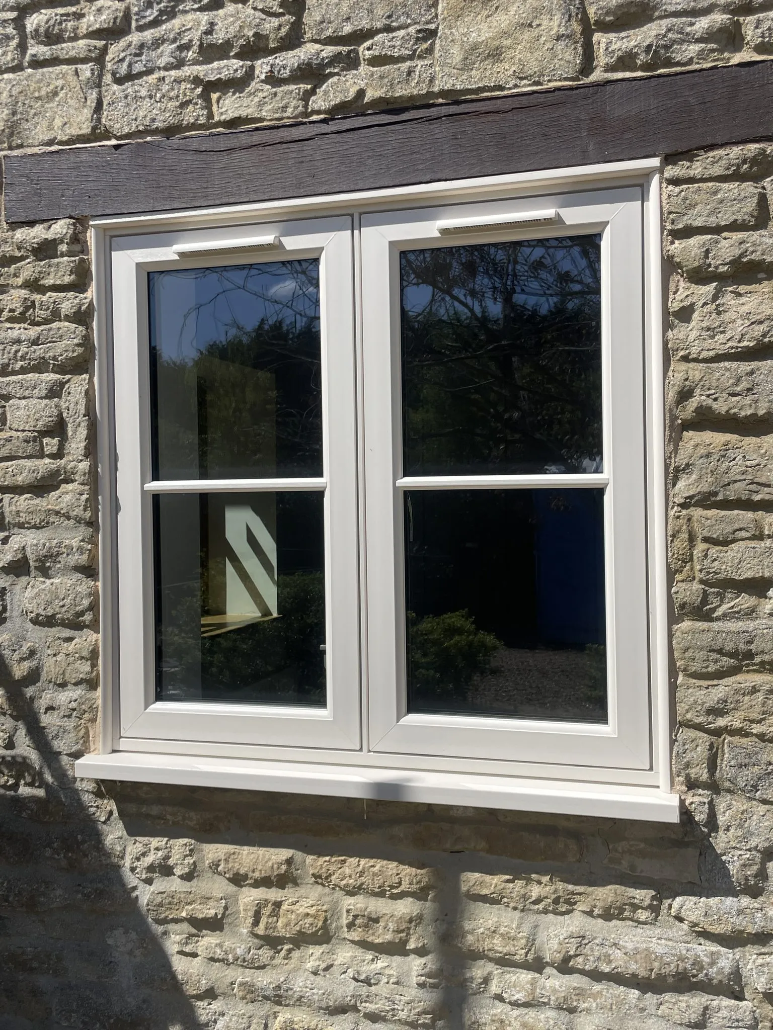Cream flush casement window with a glazing bar across each sash, fitted in a stone wall under a timber lintel.