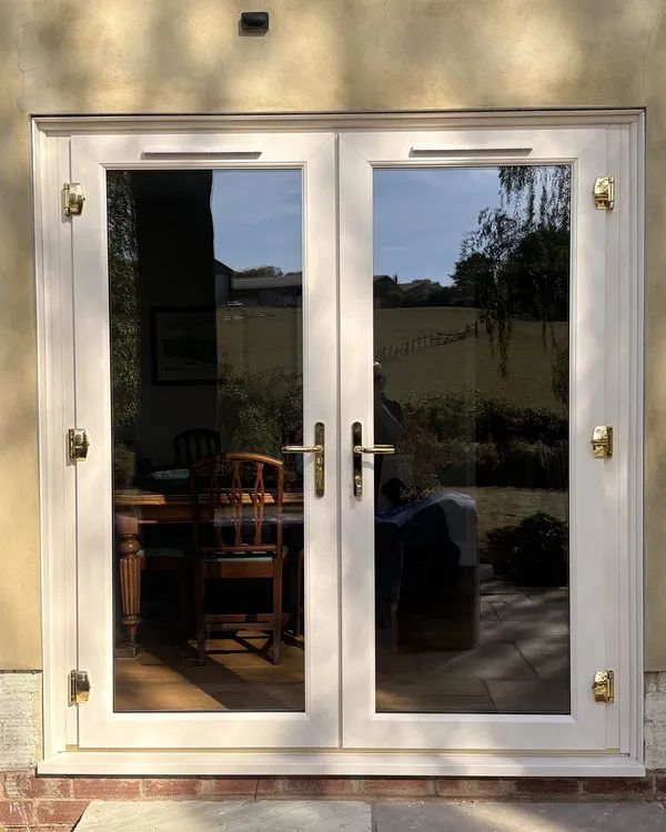 Cream uPVC French doors with brass hinges and handles, fitted in a rendered wall and opening onto a patio.