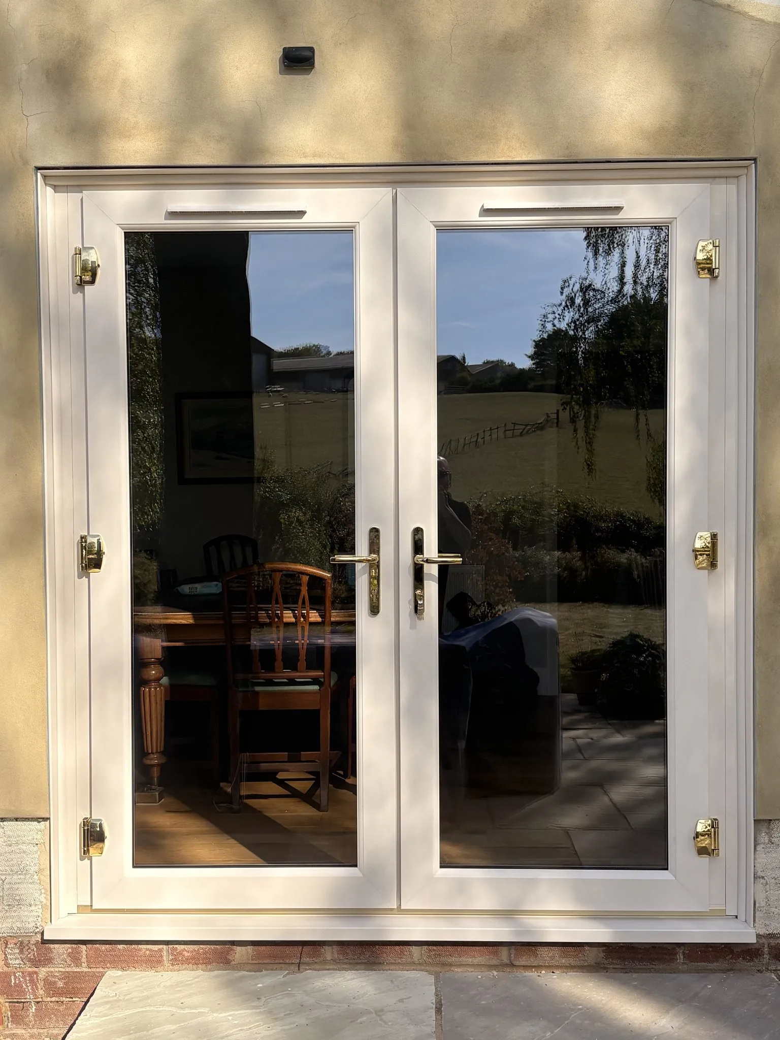 Cream uPVC French doors with brass hinges and handles, fitted in a rendered wall and opening onto a patio.