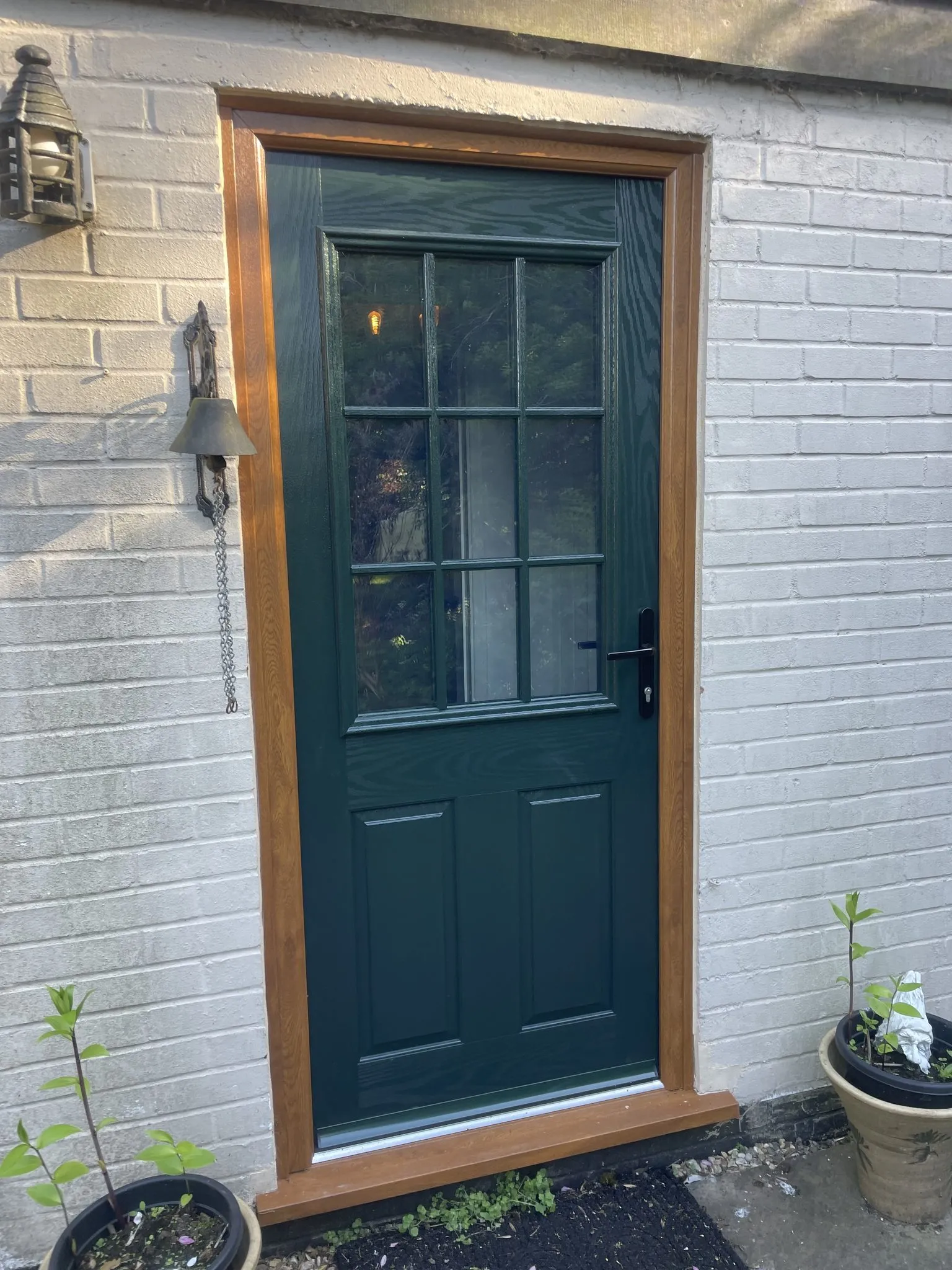 Dark green composite door with a Georgian-barred glazed top half, fitted in an oak-effect frame in a painted brick wall.