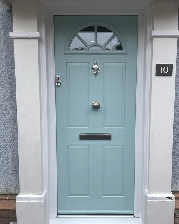Duck egg blue composite front door with a fan-shaped glazed top, chrome knocker and letterplate, framed by white pillars.
