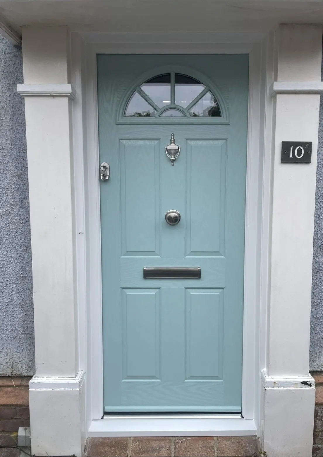 Duck egg blue composite front door with a fan-shaped glazed top, chrome knocker and letterplate, framed by white pillars.
