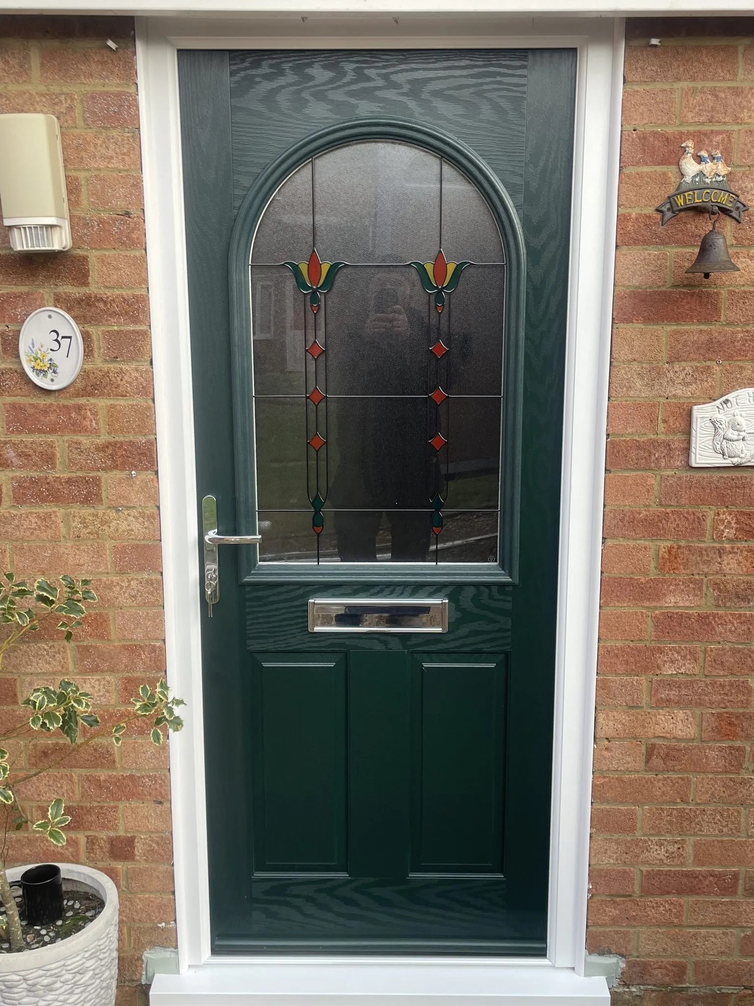 Dark green composite front door with a large arched glass panel featuring stained glass tulips, in a white frame on a brick house.