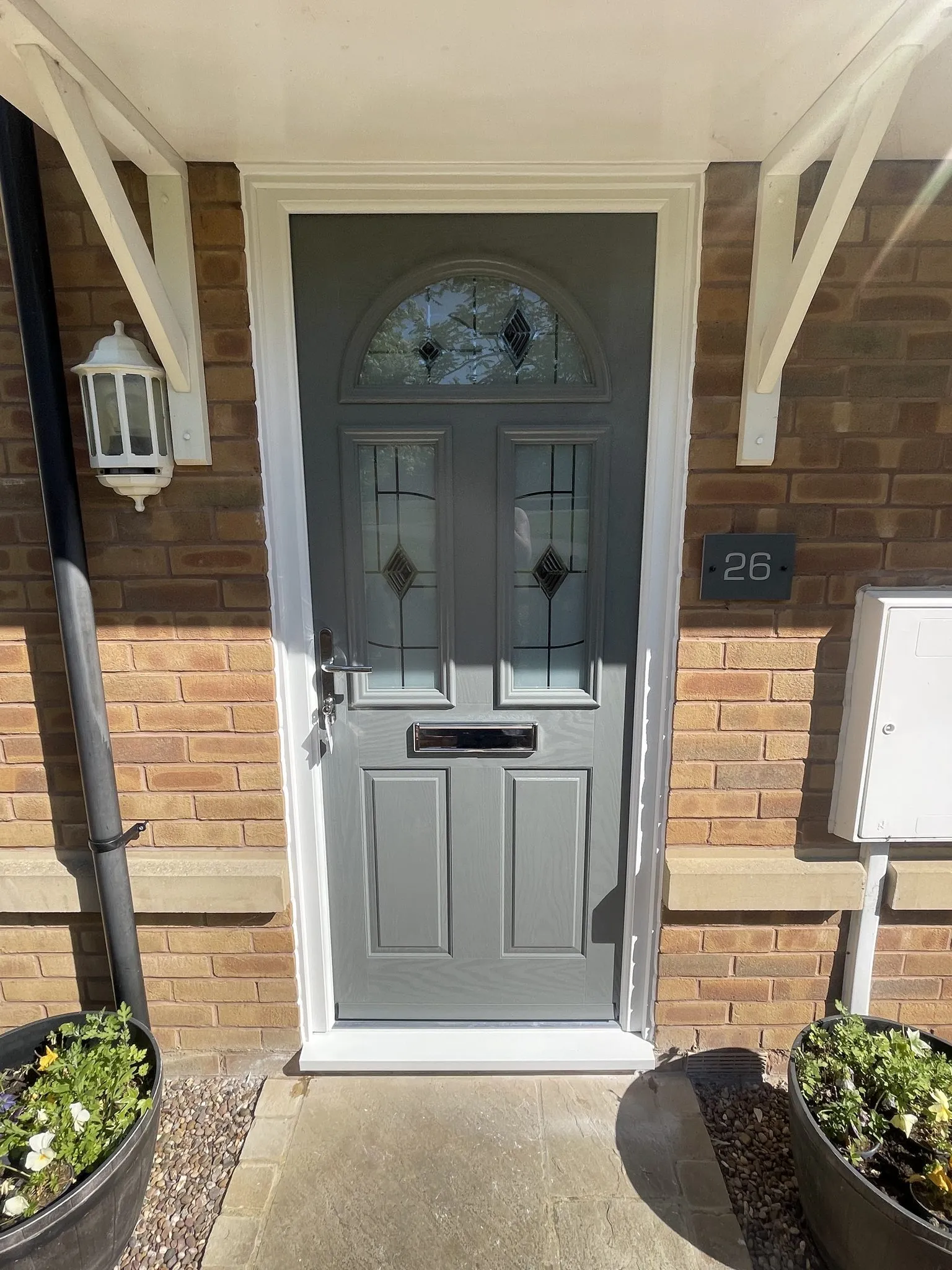 Grey composite front door with an arched decorative glass top panel and leaded glazing, in a white frame under a white canopy.
