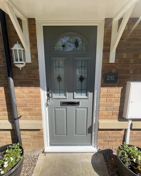 Grey composite front door with an arched decorative glass top panel and leaded glazing, in a white frame under a white canopy.