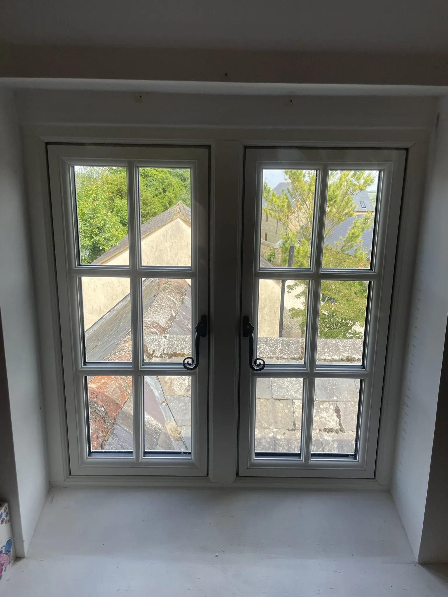 Inside view of a pair of white flush casement windows with Georgian bars and black monkey-tail handles in a deep window reveal.