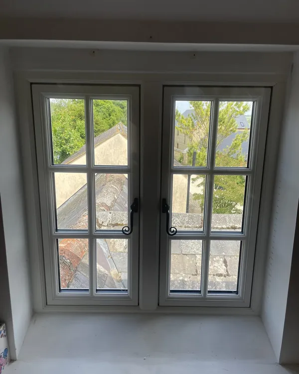 Inside view of a pair of white flush casement windows with Georgian bars and black monkey-tail handles in a deep window reveal.