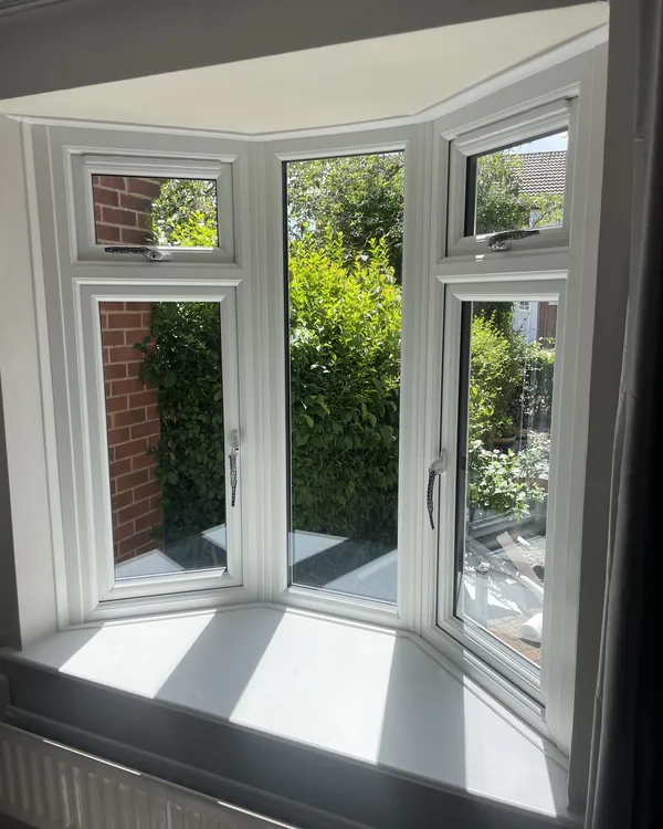 Inside view of a three-sided white uPVC bay window looking out onto a garden hedge.