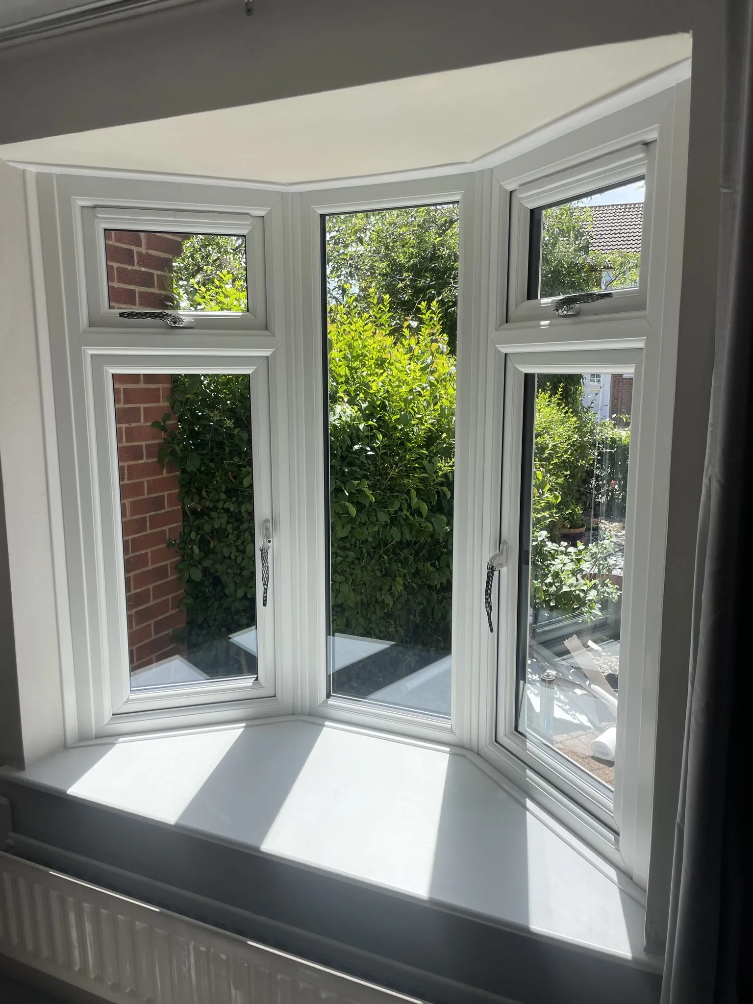 Inside view of a three-sided white uPVC bay window looking out onto a garden hedge.