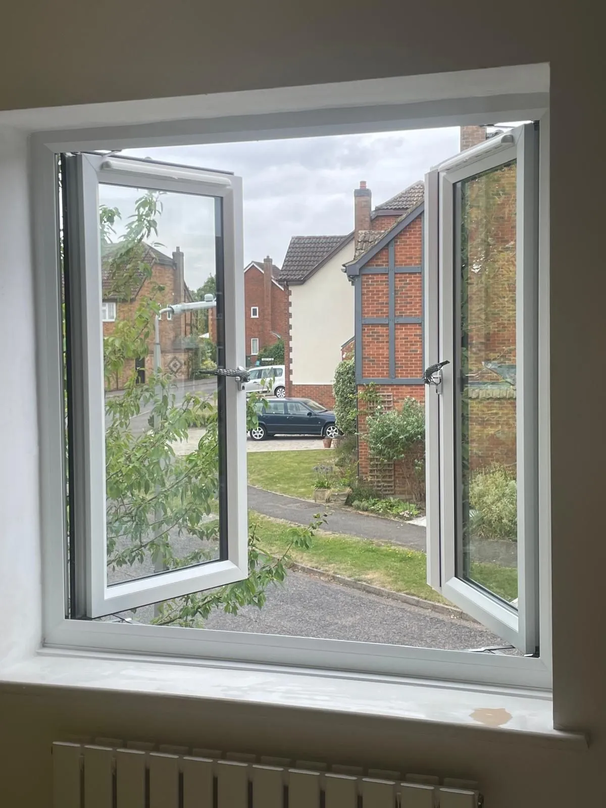 Inside view of a white uPVC window with both casements open, looking out over a residential street.