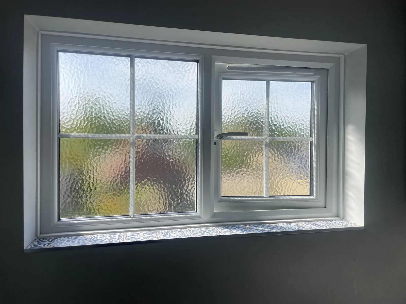 Inside view of a white uPVC casement window with Georgian bars and obscure glass, above a patterned tiled sill.