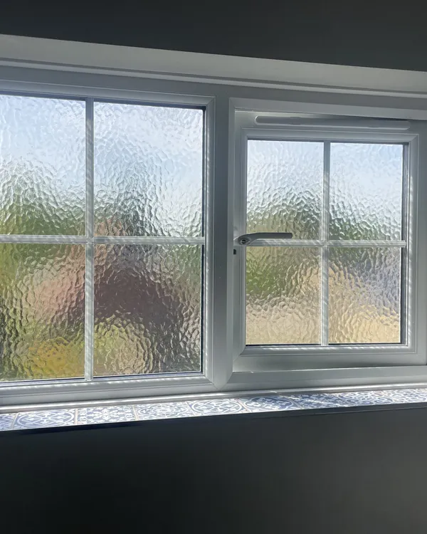 Inside view of a white uPVC casement window with Georgian bars and obscure glass, above a patterned tiled sill.