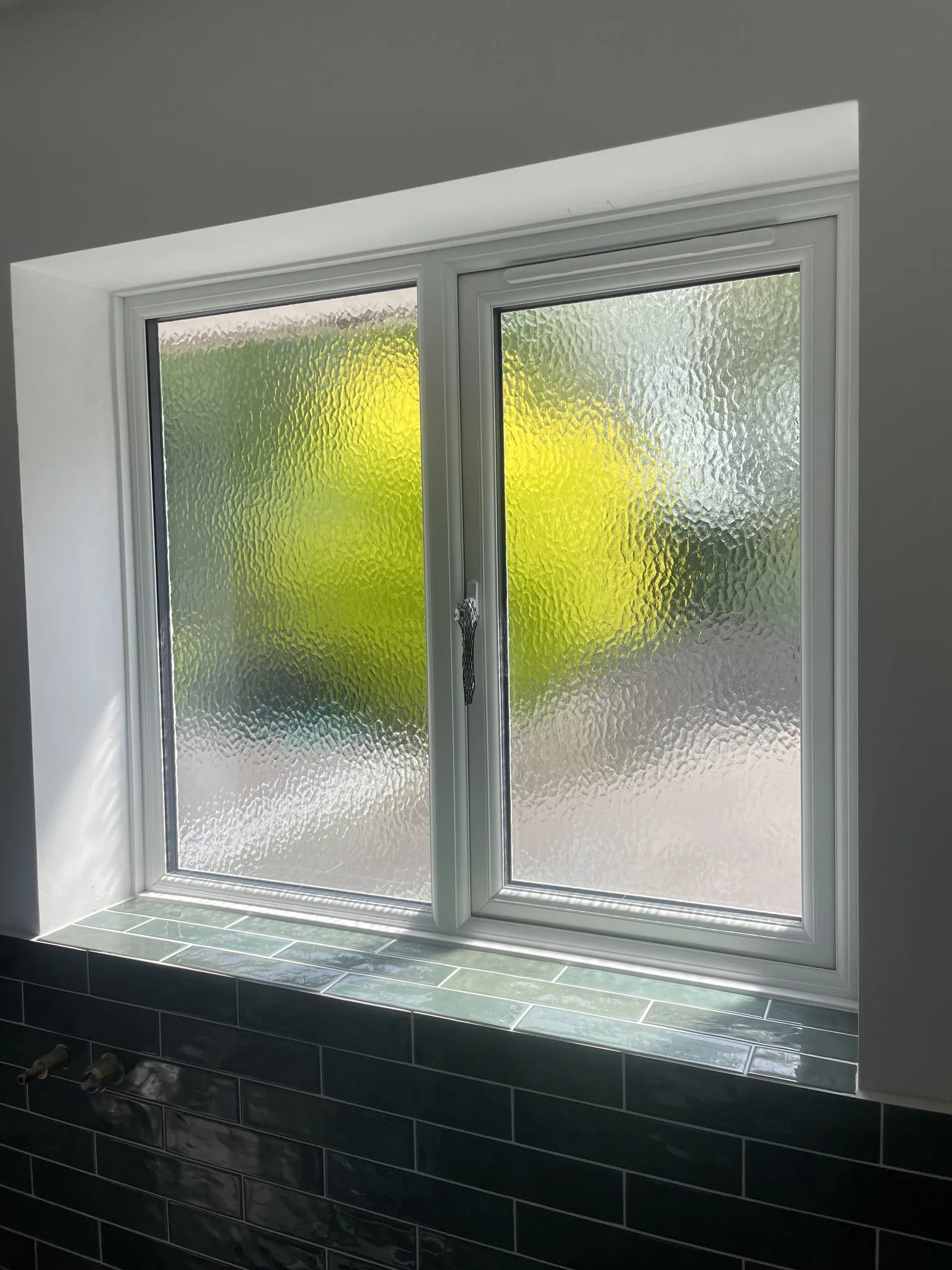 Inside view of a white uPVC casement window with obscure glass above a tiled sill.