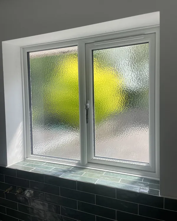 Inside view of a white uPVC casement window with obscure glass above a tiled sill.