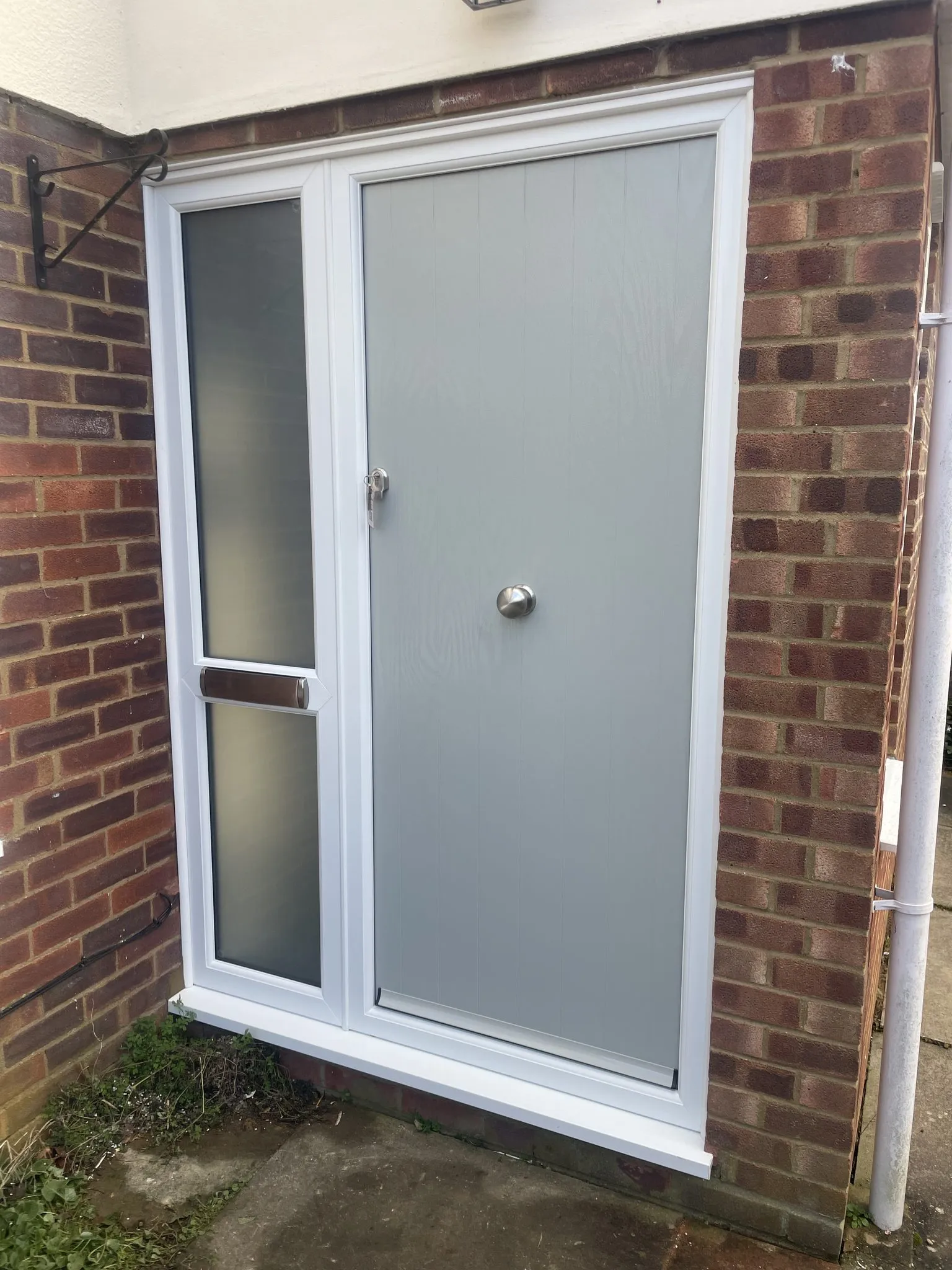 Solid light grey composite door with a centre knob, beside a white uPVC side panel with frosted glass and a letterplate.